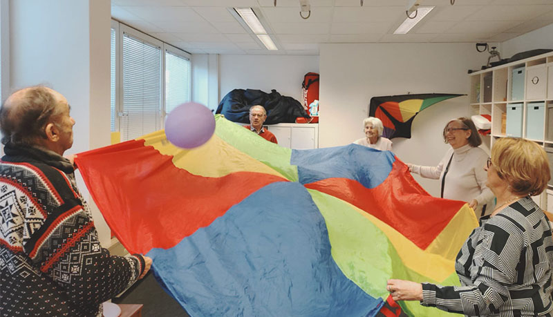 5 Menschen haben ein großes Tuch zwischen sich aufgespannt und ballancieren darauf einen Luftballon